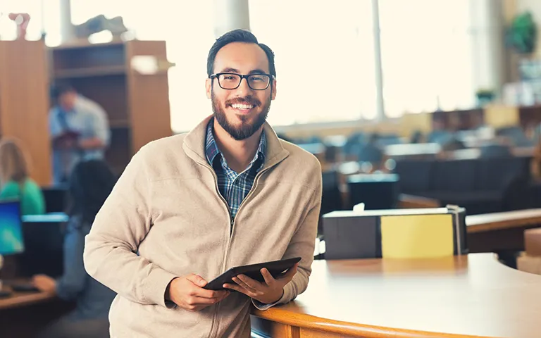 Trendy adult college student in library with digital tablet