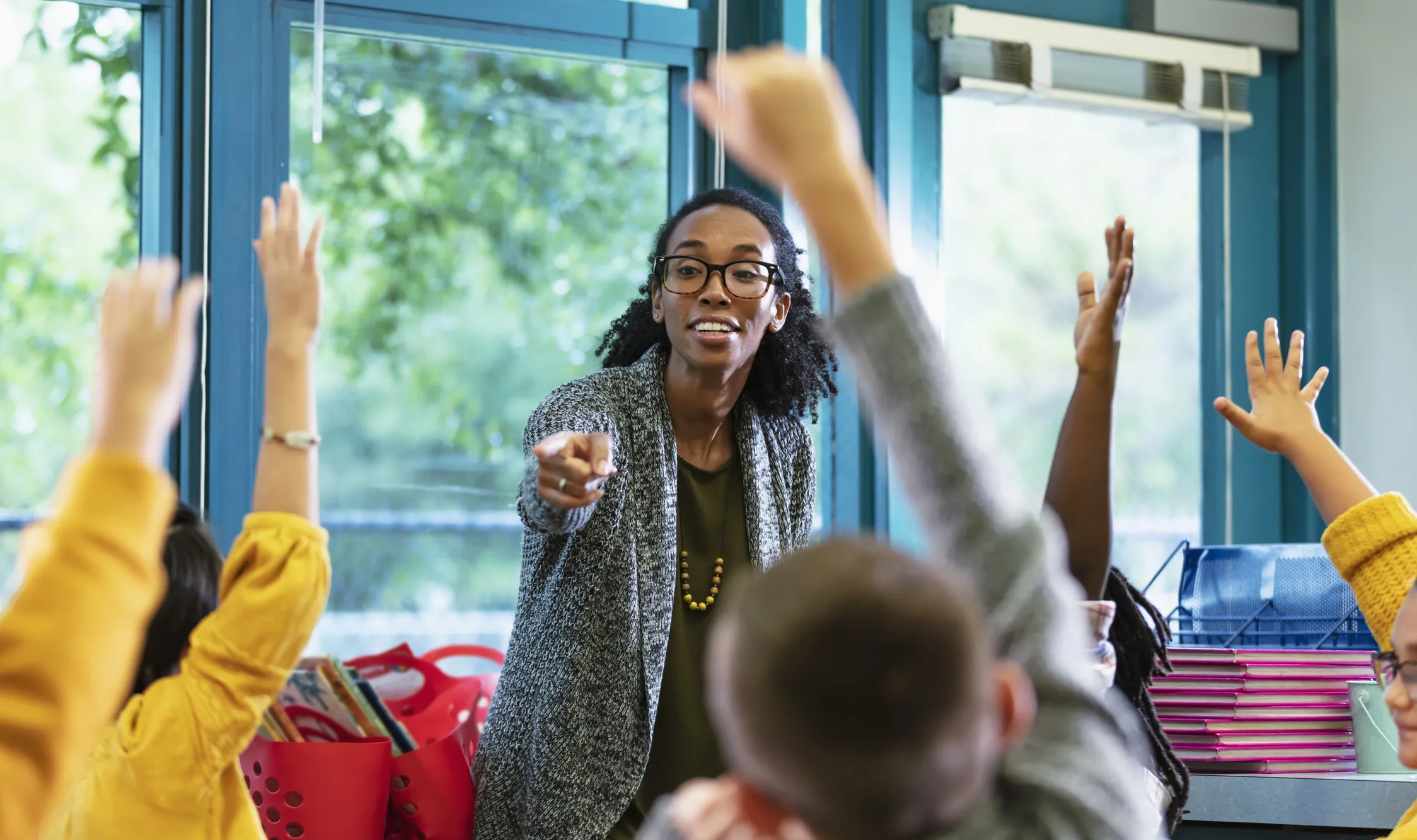 A teacher in classroom points to a student raising their hand